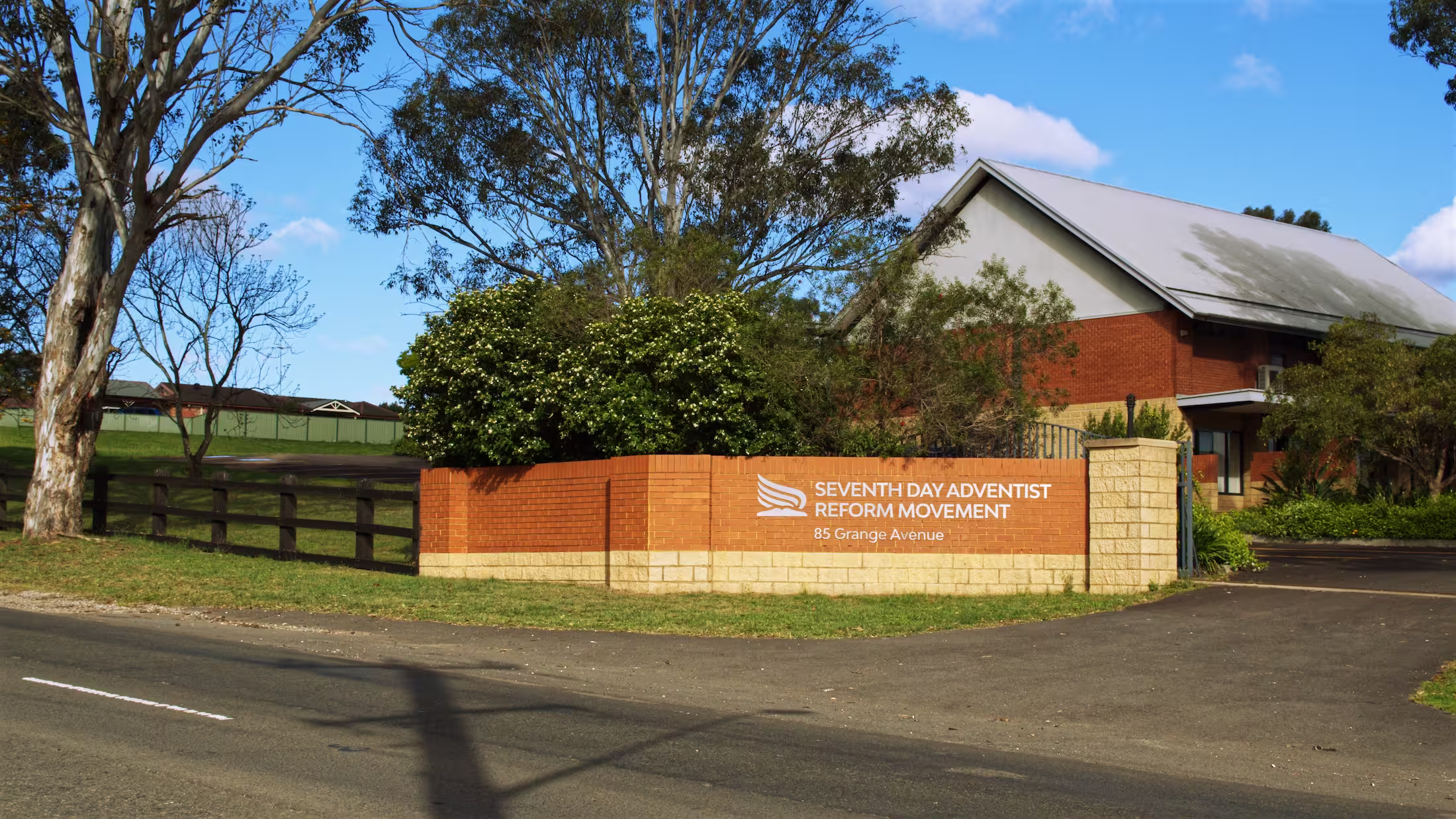 Church grounds with gum trees, a lawn and a brick entrance sign on a sunny afternoon