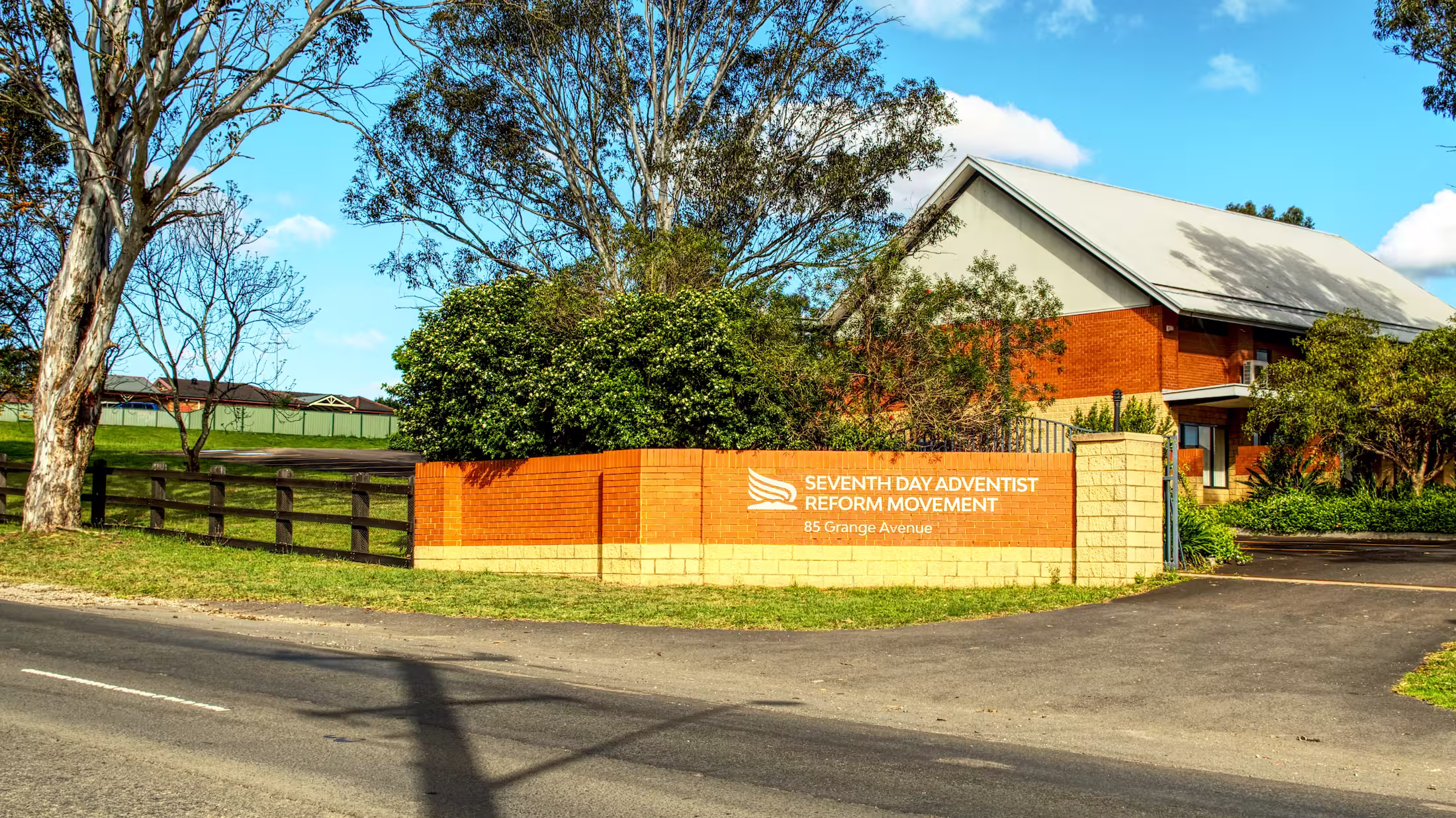 Church grounds with gum trees, a lawn and a brick entrance sign on a sunny afternoon